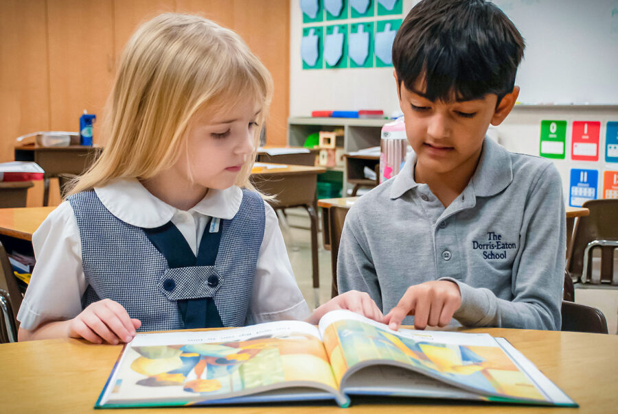 Two kindergartners sittig side by side, reading a colorful storybook.